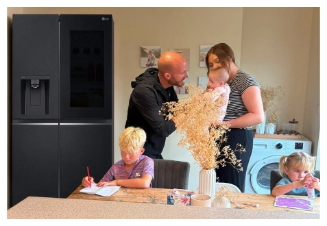 Una foto di famiglia in cucina: i genitori sistemano fiori secchi mentre tengono in braccio un bambino, con un frigorifero LG vicino e due bambini che colorano al tavolo.