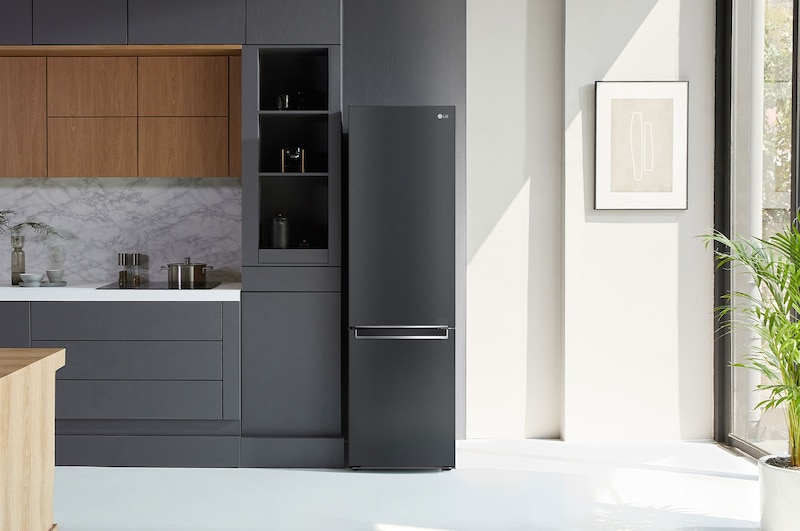 Frigorifero Combinato LG GBB72MCVBN Matte Black, integrato in una moderna cucina dai toni verdi con pavimento in legno e piante.