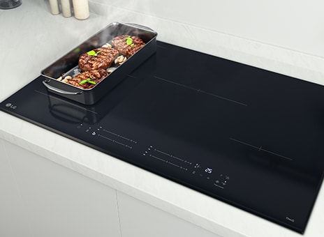 Piano cottura a induzione LG con padella nera sul lato sinistro, cuocendo bistecche e verdure con vapore.