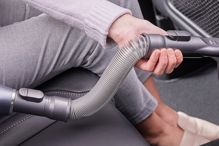 Una donna seduta in un'auto usa il tubo flessibile ed estendibile dell'aspirapolvere per raccogliere i detriti nell'auto.