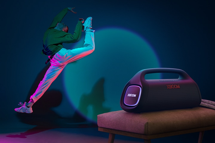 Il dispositivo LG XBOOM Go XG9 è posizionato sulla sedia. Lancia un'illuminazione da spettacolo sulla parete e una persona balla davanti.