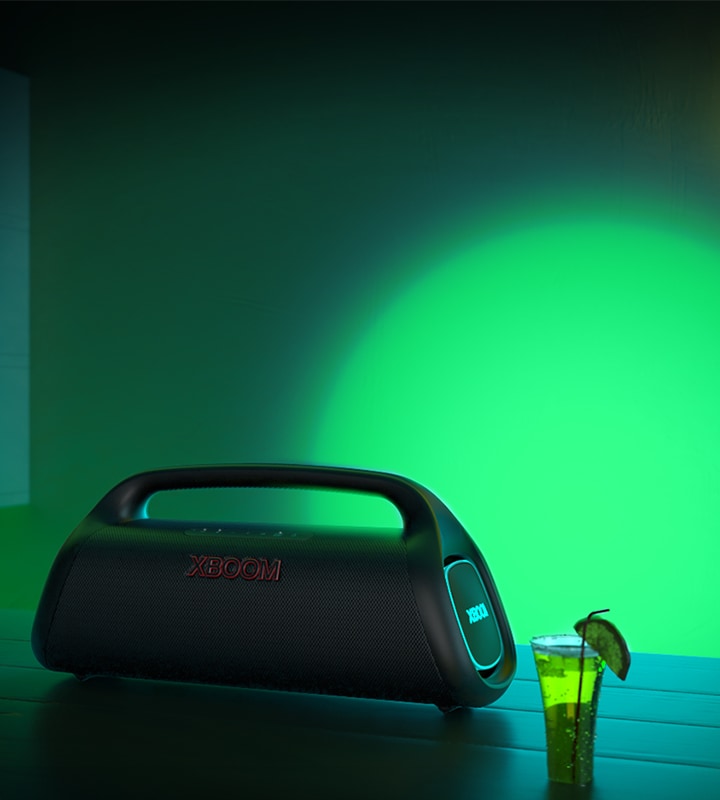 Il dispositivo LG XBOOM GO XG9 è posizionato sul tavolo di un bar. Produce un'illuminazione da spettacolo di colore verde e blu.
