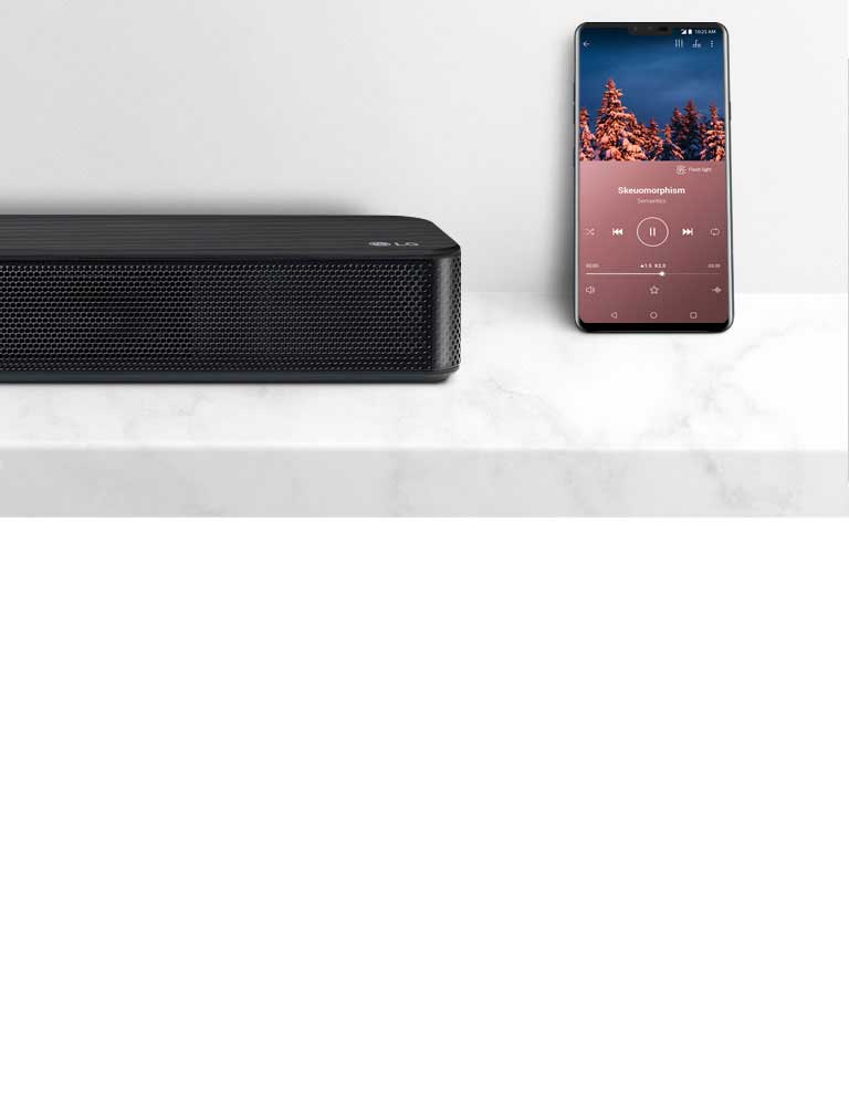Particolare del lato destro della soundbar LG accanto allo smartphone. I due dispositivi sono sul ripiano bianco.
