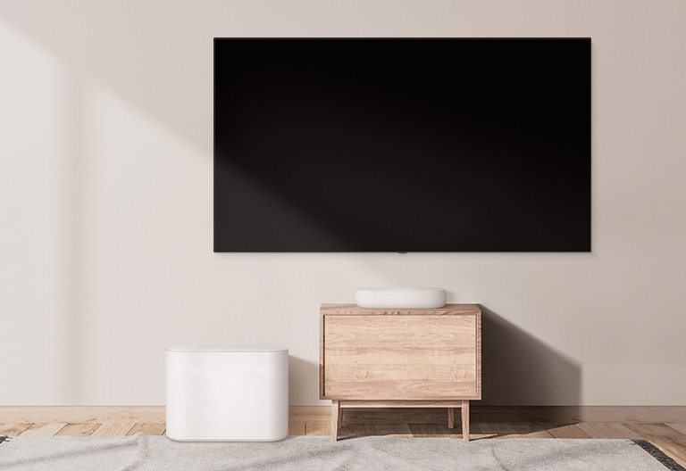 Una soundbar ingombrante si trova su un ampio mobile e sulla sua sinistra è posizionato un subwoofer. La scena cambia e una soundbar compatta compare su un mobile più piccolo con un subwoofer sulla sinistra.