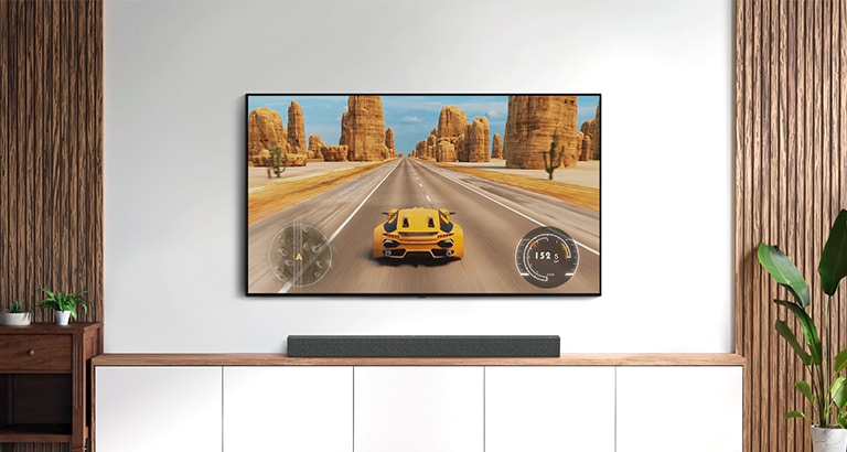 In un salotto bianco ci sono un TV e una soundbar. Su uno schermo TV (riprodurre il video) ci sono delle corse d’auto.