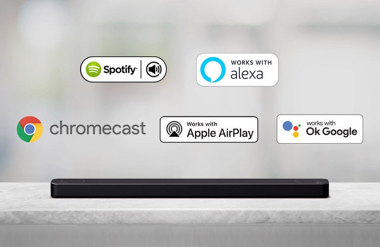 Una soundbar è posizionata su un ripiano grigio con i loghi della piattaforma AI – da sinistra a destra: Spotify, Alexa, Chromecast, Apple Airplay e OK Google.
