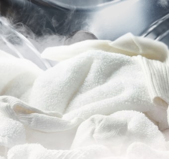 Foto di indumenti bianchi all'interno dell'oblò con del vapore intorno.