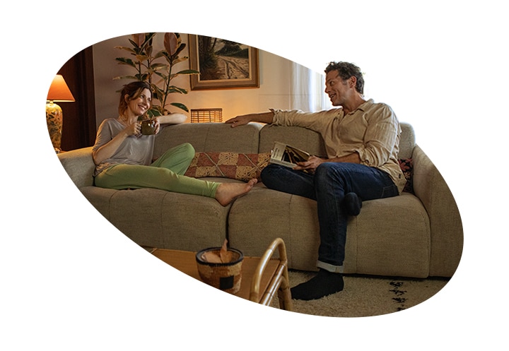 Una donna e un uomo adulti sono seduti su un divano di casa e parlano sorridendo.