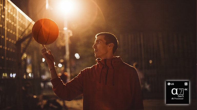 Un uomo in un campo da basket di sera fa ruotare il pallone sul dito.