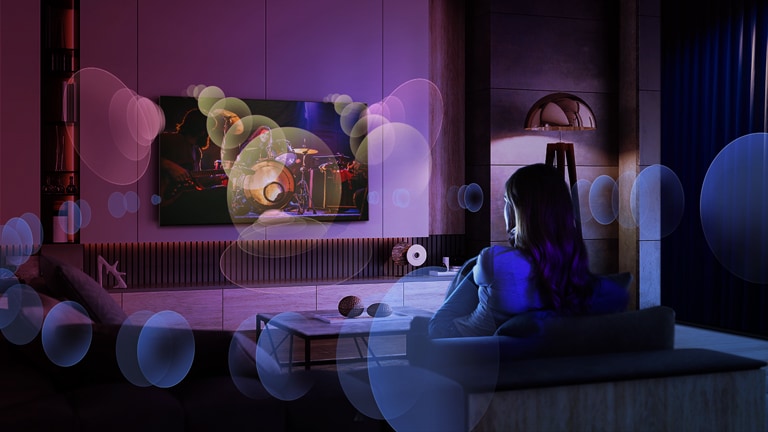 Una donna guarda un concerto seduta su un divano e intorno a lei bolle che rappresentano l’audio surround