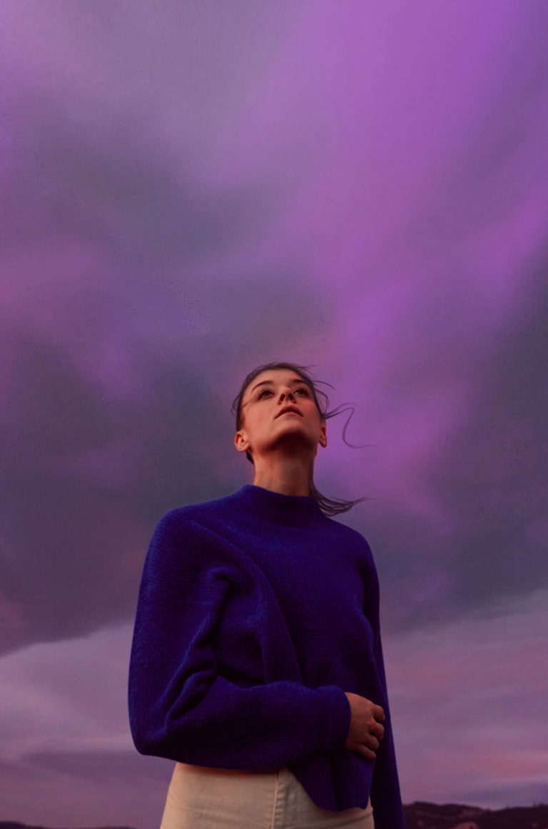 Una donna osserva il cielo viola. I suoi capelli ondeggiano lievemente.