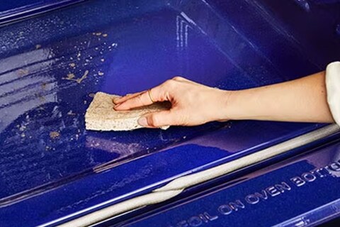 Immagine di una mano che pulisce il forno con una spugna.