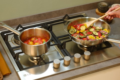 Immagine di un piano cottura a gas su cui c'è un pentolino e una piastra e  una padella.