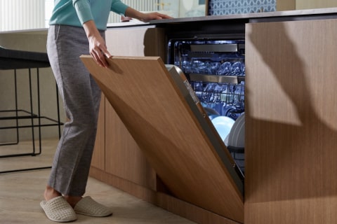 Immagine di una lavastoglie integrata nell'arredamentod della cucina. La porta è semi-aperta e una donna la sta chiudendo.