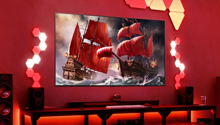 Una vivace configurazione di gioco con un grande schermo che mostra una battaglia tra navi pirata. La stanza è illuminata con luci ambientali rosse e luci esagonali a parete.