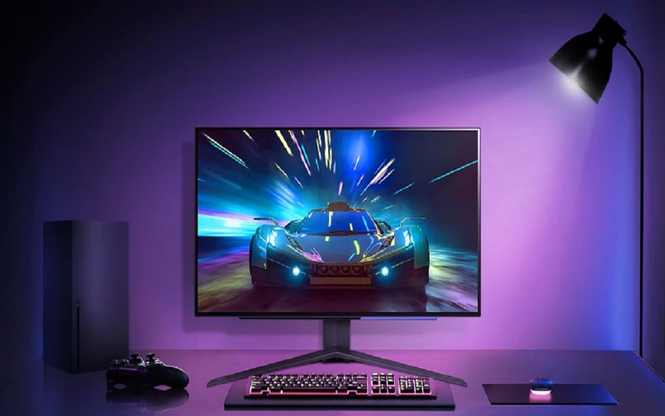 Una postazione da gaming con un monitor elegante che mostra un gioco di corse futuristico, illuminata da luci ambientali viola.