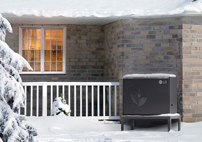 Un paesaggio invernale coperto di neve, con un'unità di climatizzazione LG all'esterno di una casa di mattoni, mentre la neve ricopre il tetto e parte dell'unità.