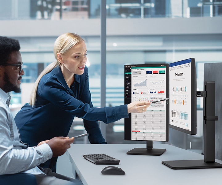 Due impiegati, un uomo e una donna, discutono guardando il monitor in ufficio.