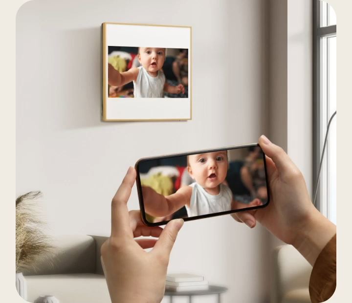 Una persona fotografa una cornice appesa al muro con uno smartphone, vicino a una finestra e sopra un divano.