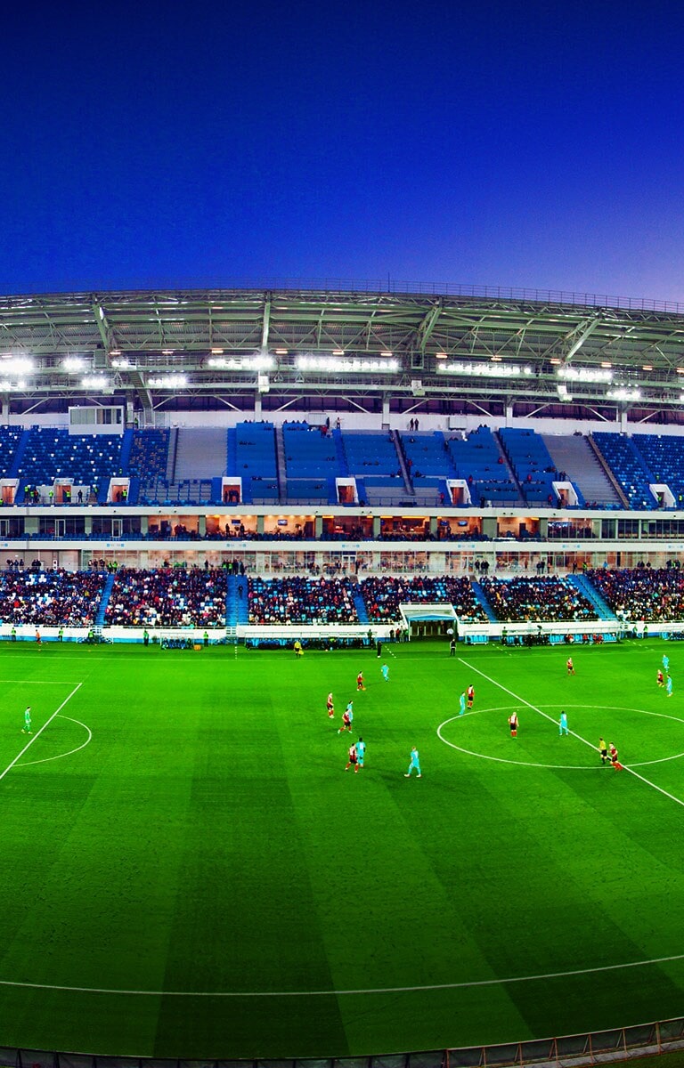 Vista grandangolare di uno stadio di calcio pieno di tifosi che guardano la partita in corso.