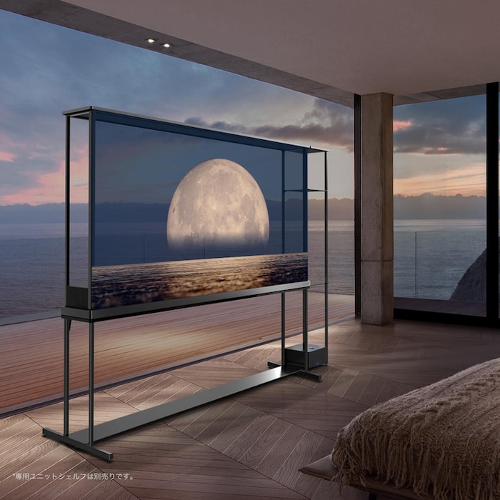 透明スクリーンで海岸の上に浮かぶ月を映し出すLG SIGNATURE OLED T。海を臨むを映し出し、部屋の真ん中にたたずむLG SIGNATURE OLED T。右側にはベッドとラウンジチェア。