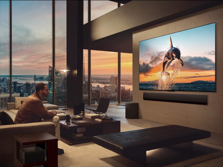 都市の風景を臨むゆったりとしたリビングルーム。LG OLED TVがスタンドに設置されている。超薄型設計であるため、没入感が高い画面。Zero Connect Boxが見えるが、隠されてはいない。