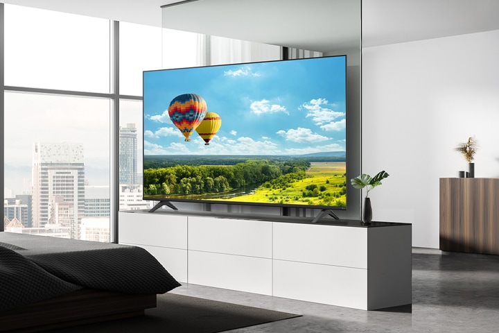 A TV is installed in a hotel room, displaying a vivid landscape of a green field with hot air balloons under a clear blue sky.