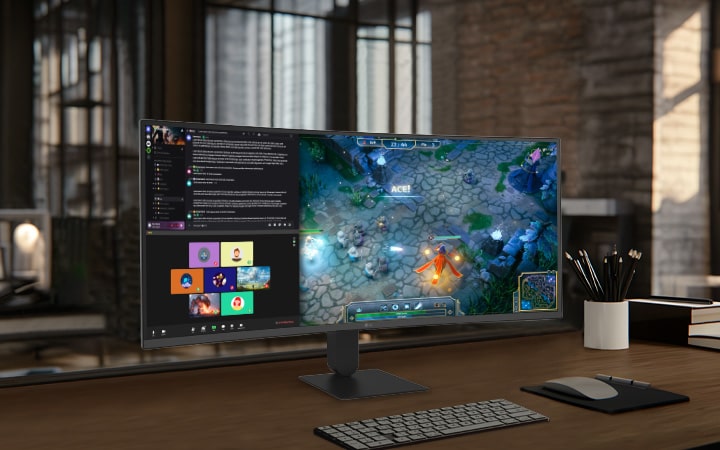 A modern home office setup featuring a large ultra-wide LG monitor displaying data dashboards and graphs, with a wireless keyboard and mouse on a wooden desk.	