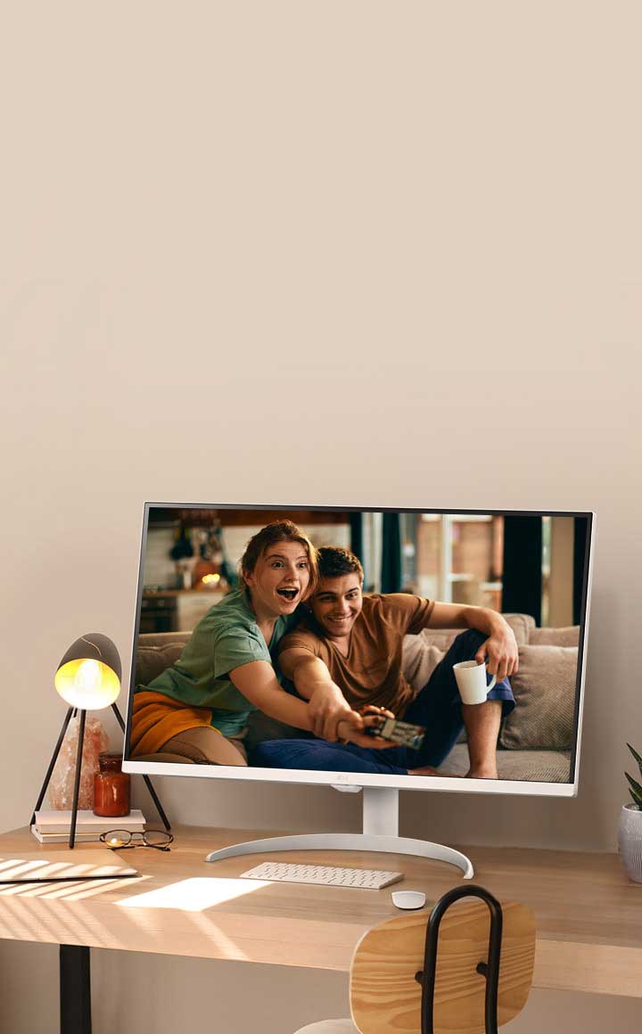 太陽光が入る窓のそばのデスクにSmart Monitorが設置され、映画を再生している。モニターの横にはランプと鉢植えの植物がある。デスクの上にはキーボードとマウスが置かれている。