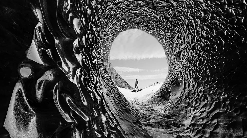 洞窟のようなトンネルの中をハイキングする男性の動画。スライダーが画面上を移動し、画像に無限のコントラストが適用される。