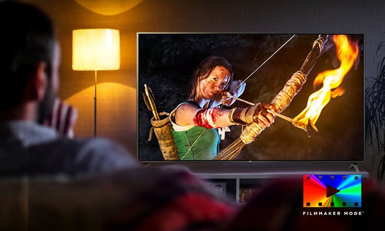 Мужчина сидит на диване, смотрит фильм в жанре экшн. Девушка на экране держит в руках натянутый лук и стрелу.