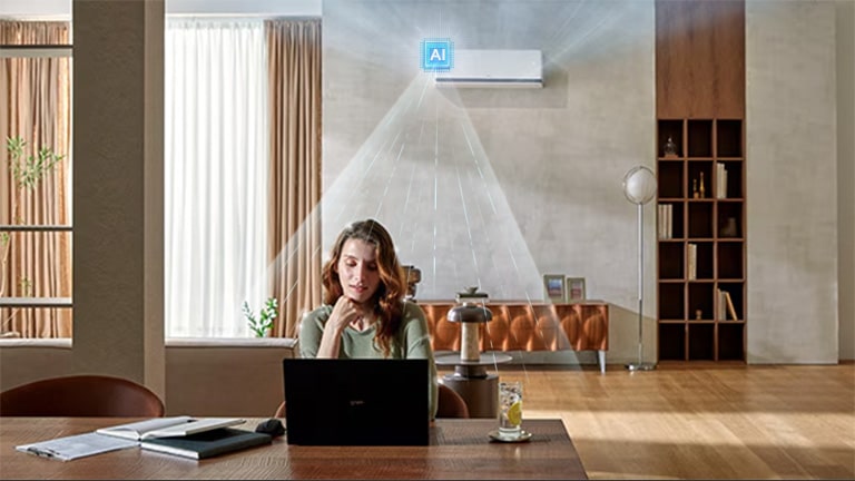 LG DUALCOOL AI air conditioner cooling a woman working at a desk with a laptop in a living room.