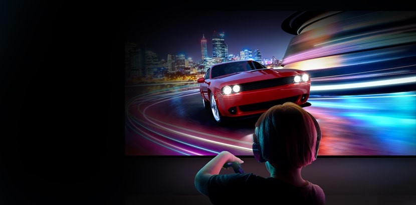 Артқы жағында құлаққап киген баланың үлкен LG теледидарында жарыс ойынын ойнап жатқаны көрсетілген.