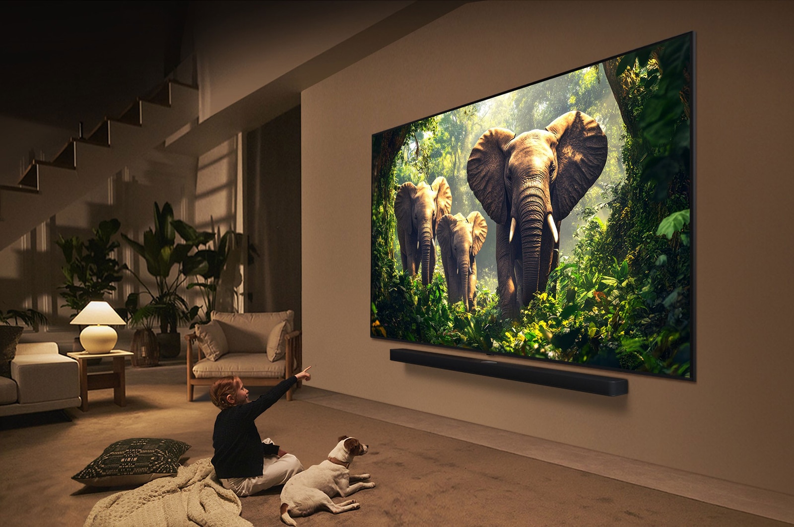 A girl and a dog are seated in front of a LG QNED TV mounted on a wall depicting three elephants walking outwards above a LG Soundbar. The title talks about how every action is more thrilling on a massive screen.