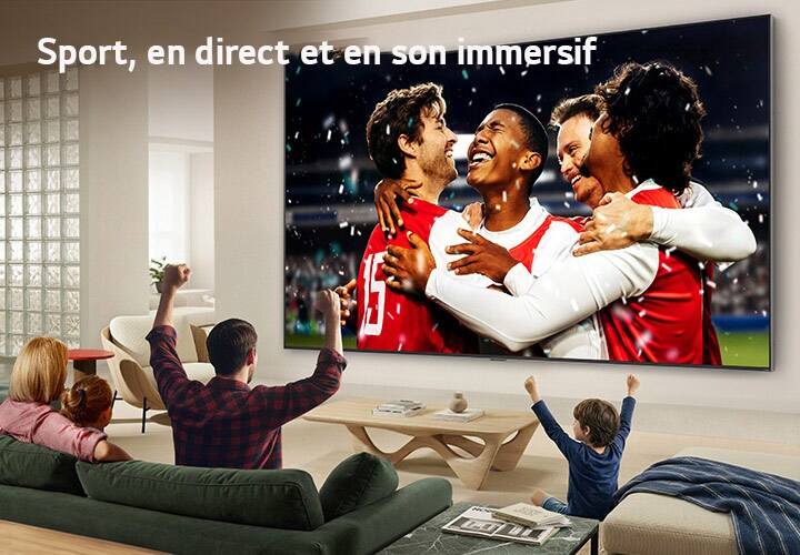 Le LG Ultra Big TV fixé au mur dans un salon lumineux montre une célébration de sport dans un stade avec des couleurs vives et une qualité d'image raffinée sur un grand écran, tandis qu'une famille assise sur des canapés applaudit ensemble.