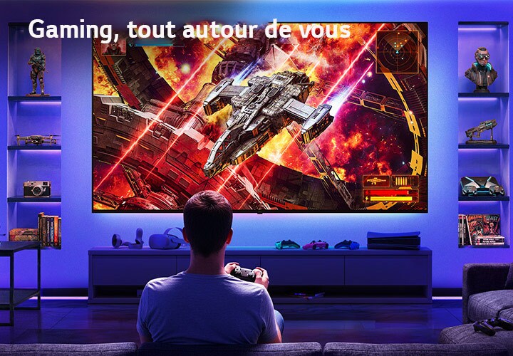 LG Ultra Big TV est fixé au mur dans une salle de jeux éclairée au néon, où un grand écran montre une scène de bataille spatiale éclatante tandis qu'un joueur est assis face à l'écran, illustrant une expérience de jeu immersive et captivante.