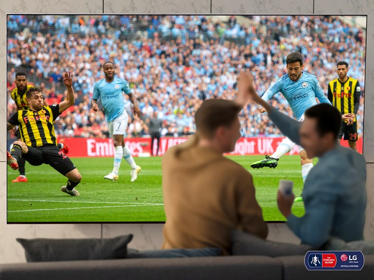 Deux hommes applaudissent en regardant un match de football sur un téléviseur NanoCell dans un salon. 