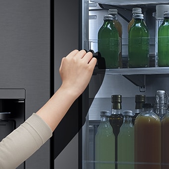 La vue avant du réfrigérateur à verre noir InstaView avec de la lumière à l’intérieur. Des mains qui appuient sur l’écran InstaView.