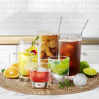 Une personne tient un verre contenant une boisson dans une main et se sert une boule de glace Craft ice dans l’autre main.