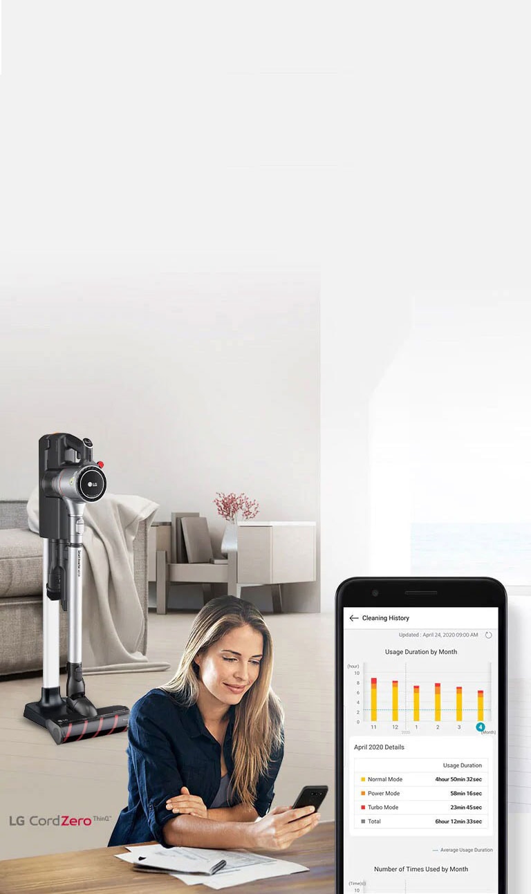 L'aspirateur sur son support est dans le salon derrière une femme qui utilise l'app ThinQ sur son smartphone.