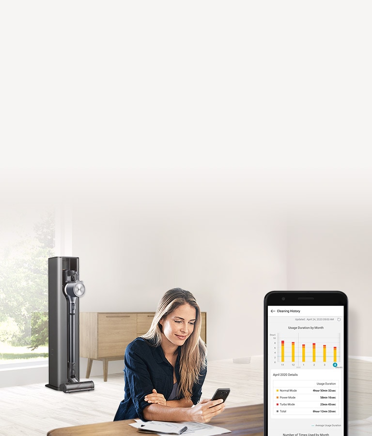 Un aspirateur est placé en arrière-plan et une femme utilise l’application ThinQ sur son smartphone.