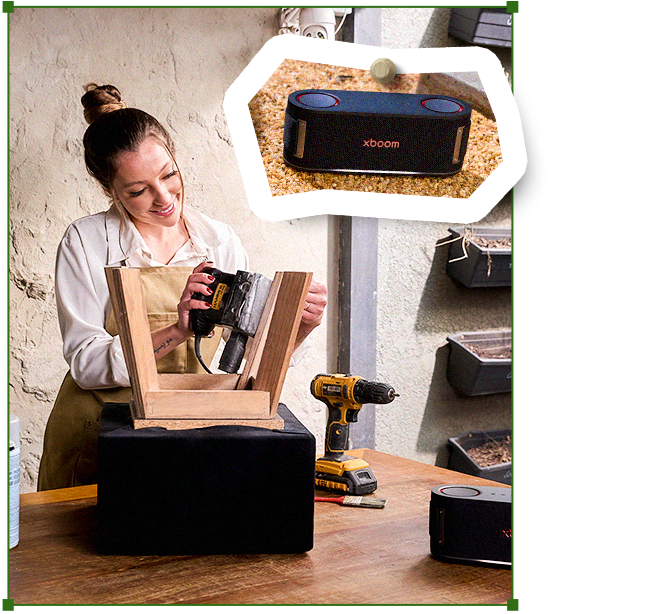 Carol reparando una silla de madera en su banco de trabajo, con un altavoz LG XBOOM cerca y herramientas sobre la mesa.