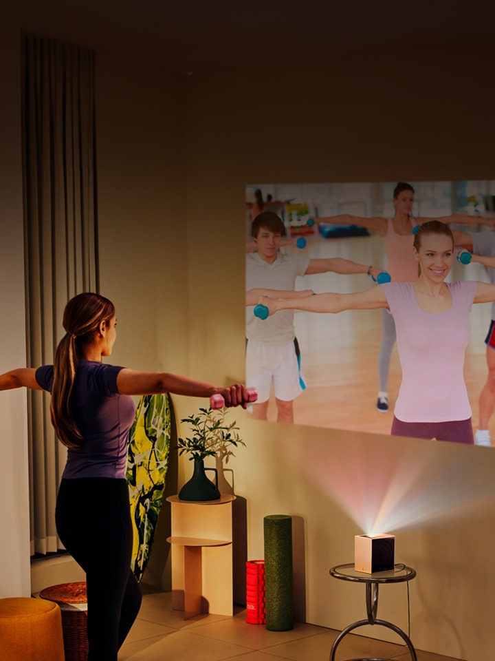 Mujer haciendo yoga con proyección LG CineBeam de fondo.
