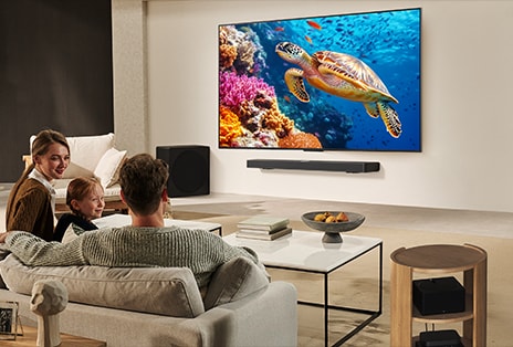 Una familia sentada en un sofá frente a un televisor LG montado en la pared, sobre una barra de sonido LG. Zero Connect Box se encuentra dentro de una mesa de centro.