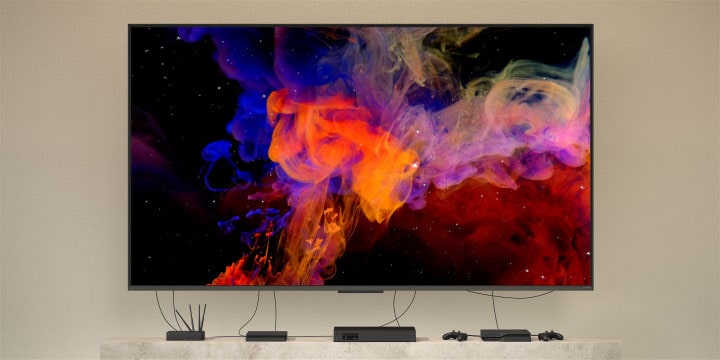 Primer plano de un QNED9M montado en la pared y conectado a varios dispositivos. Los cables y dispositivos se difuminan, dejando solo el QNED9M montado en la pared. El zoom se aleja para mostrar el QNED9M instalado en una casa moderna. La Zero Connect Box está sobre una mesa de centro.