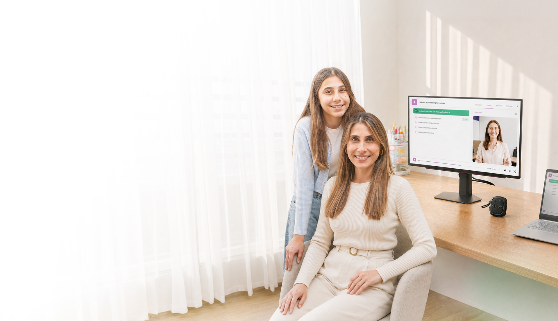 Madre sentada e hija de pie sonriendo en un escritorio iluminado con monitor LG, bocina xboom y laptop