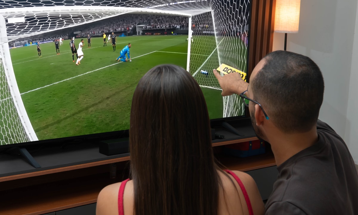 Rapael viendo un partido de fútbol con un amigo y señalando la pantalla de la TV
