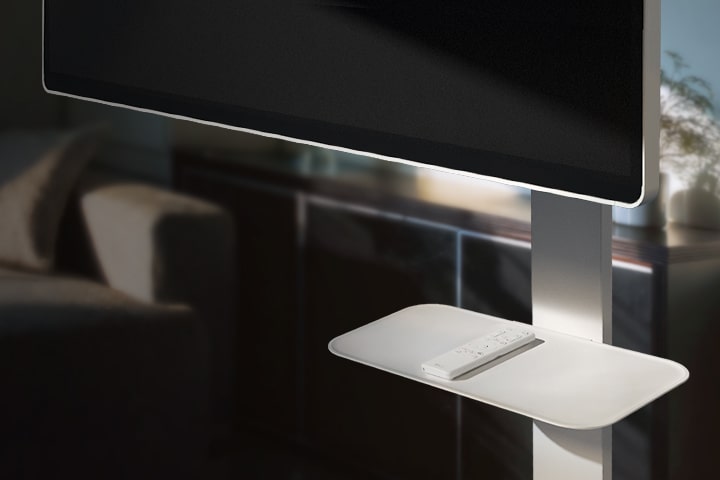Placa del soporte giratorio del LG Smart Monitor que muestra un control remoto, colocada en un acogedor salón. 