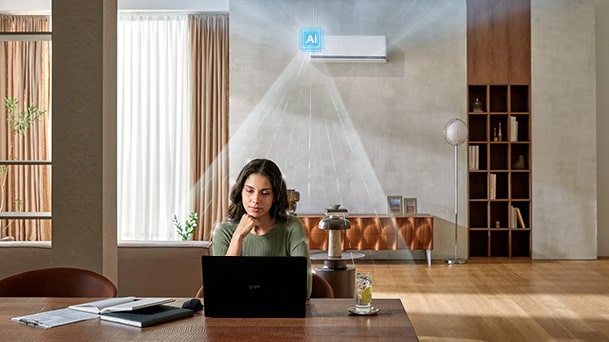  Aire acondicionado LG DUALCOOL AI refrescando a una mujer que trabaja en un escritorio con una computadora portátil en una sala de estar.