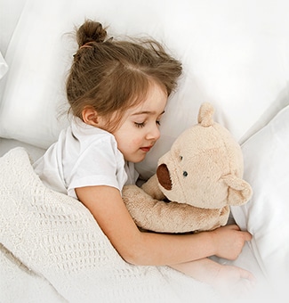 Una niña está tumbada en la cama con una muñeca en brazos